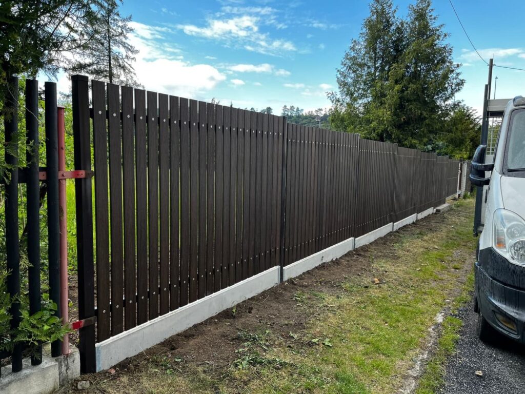Hnědý dřevoplastový plot na betonové podezdívce ukazuje možnost kombinovat různé materiály a vytvořit oplocení, které poskytuje soukromí bez nutnosti pravidelných nátěrů.